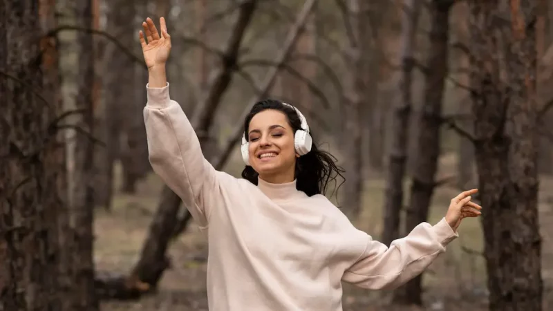 Femme souriante écoutant de la musique au casque en pleine nature, symbole d’harmonie, de paix intérieure et d’équilibre du type 9 le médiateur.