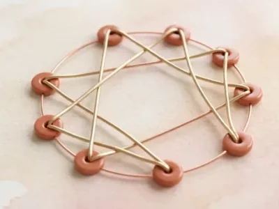 Représentation graphique du symbole de l'ennéagramme en métal doré et perles terracotta sur fond aquarelle rosé.