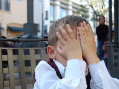 Enfant se cachant le visage avec les mains en public - illustration de la peur du jugement et de la honte ressenties dès l'enfance