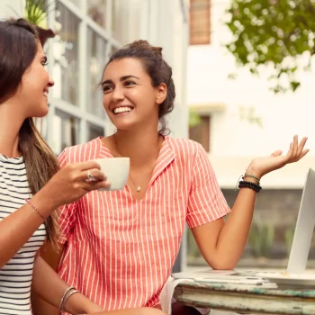 Coaching de vie en communication : deux femmes échangent autour d’un café avec le sourire, symbole d’écoute, de dialogue authentique et de relations apaisées.
